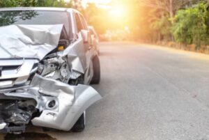 Image of a car with severe front-end damage, representing the aftermath of a car accident. The image also includes a sign for a car rental agency in the background, symbolizing the process of obtaining a replacement hire car for motor vehicle property damages.